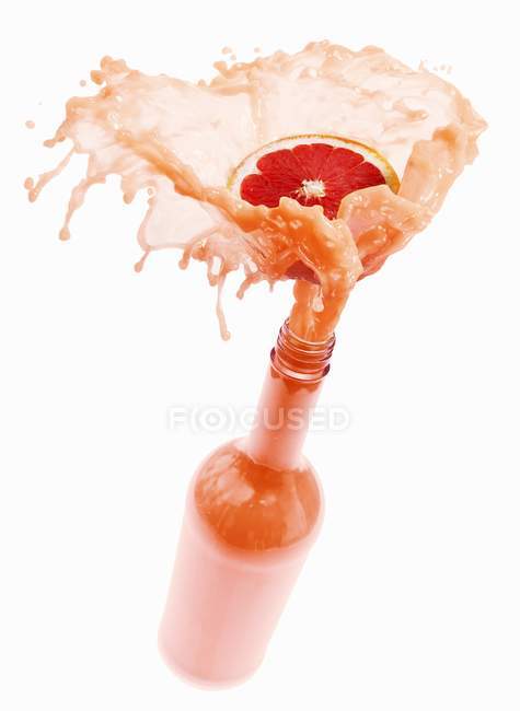 Grapefruit juice splashing out of bottle — Stock Photo
