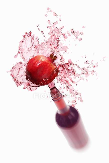 Pomegranate juice splashing out of bottle — Stock Photo