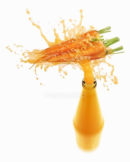 Carrot juice splashing out of bottle — Stock Photo