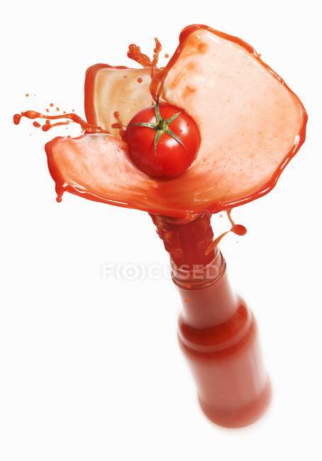 Tomato juice splashing out of bottle — Stock Photo