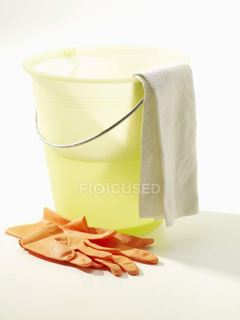 Secchio per la pulizia giallo con acqua, guanti e panno su superficie bianca — Foto stock