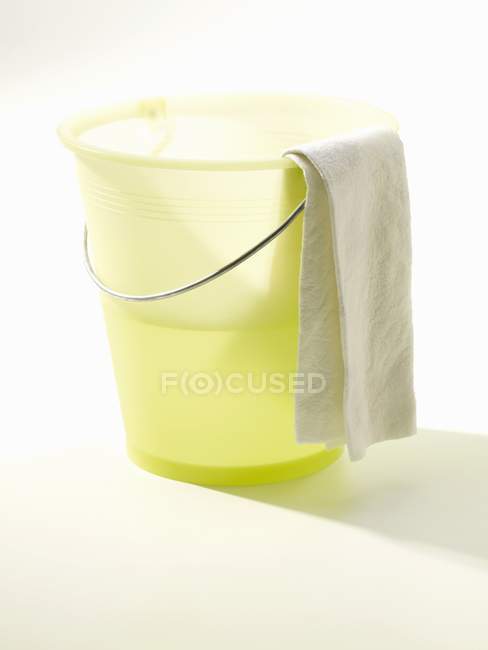 Balde de limpeza amarelo com água e pano na superfície branca — Fotografia de Stock