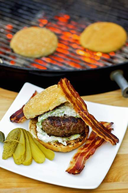 Barbecued hamburger with bacon and gherkin — Stock Photo