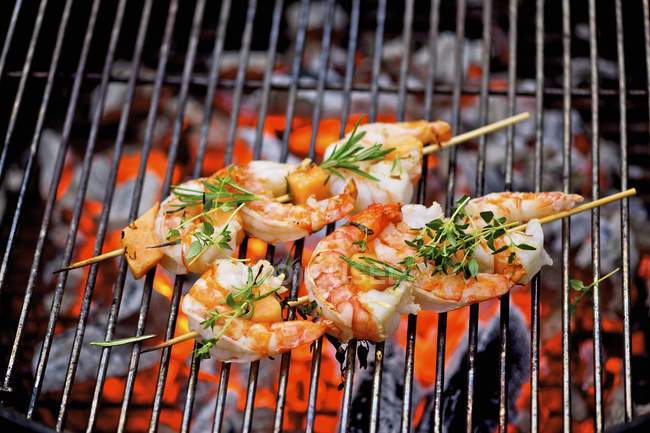 Closeup view of barbecued prawn skewers with herbs on grating over embers — Stock Photo