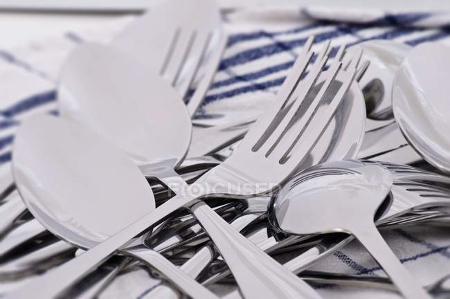 Closeup view of spoons and forks in heap on tea towel — Stock Photo