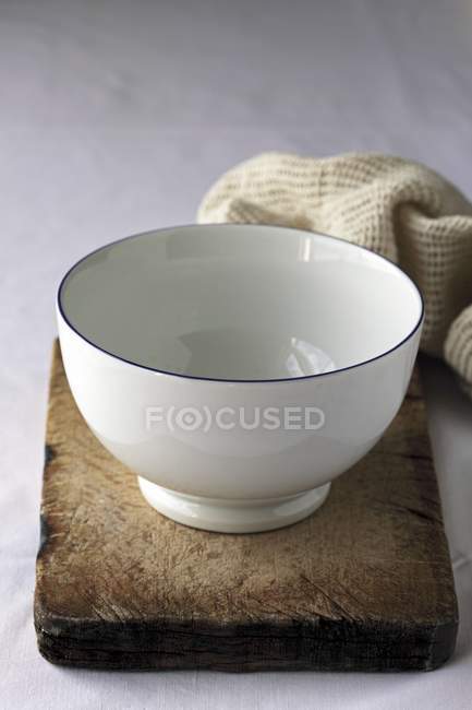 Closeup view of a white bowl on an old wooden board by towel — Stock Photo