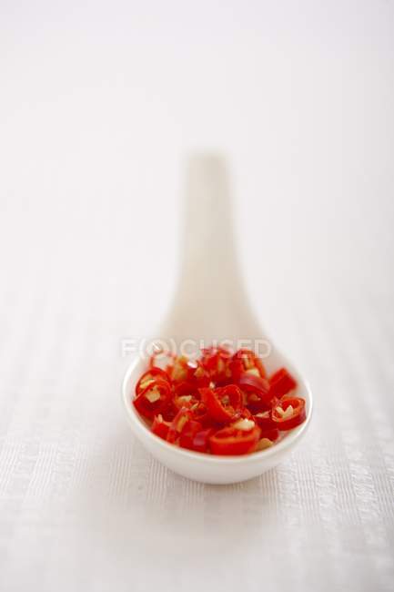 Chili rojo rebanado en cuchara blanca sobre superficie blanca - foto de stock