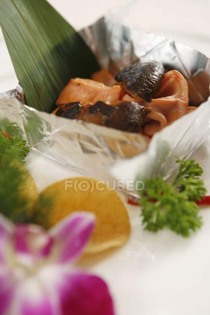 Vue rapprochée des champignons et des morceaux de poisson dans le boîtier en papier d'aluminium par des herbes et des copeaux — Photo de stock