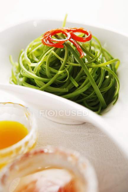 Vue rapprochée des fils de concombre vert dans un bol et des sauces — Photo de stock