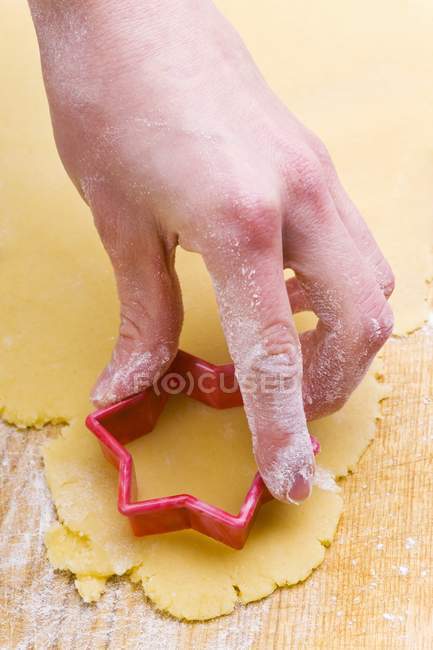 Closeup view of hand cutting out a biscuit with a star-shaped cutter — Stock Photo