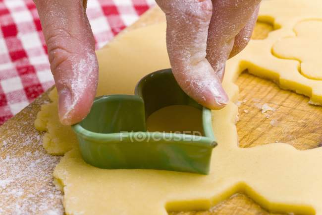 Closeup view of hand cutting out a biscuit dough with a heart-shaped cutter — Stock Photo