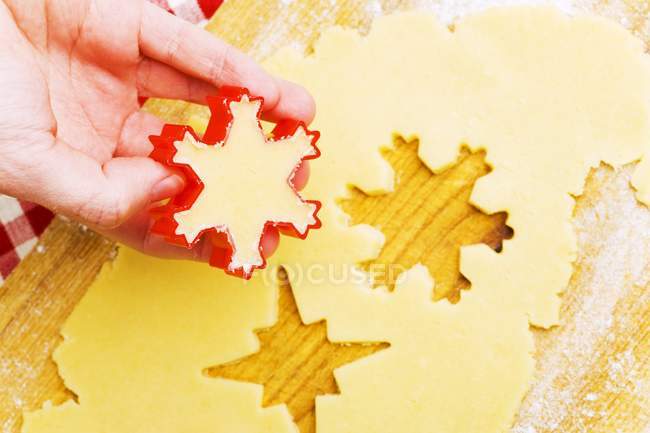 Nahaufnahme ausgeschnittene Ansicht von Hand beim Ausschneiden von Keksen aus Biskuitteig — Stockfoto