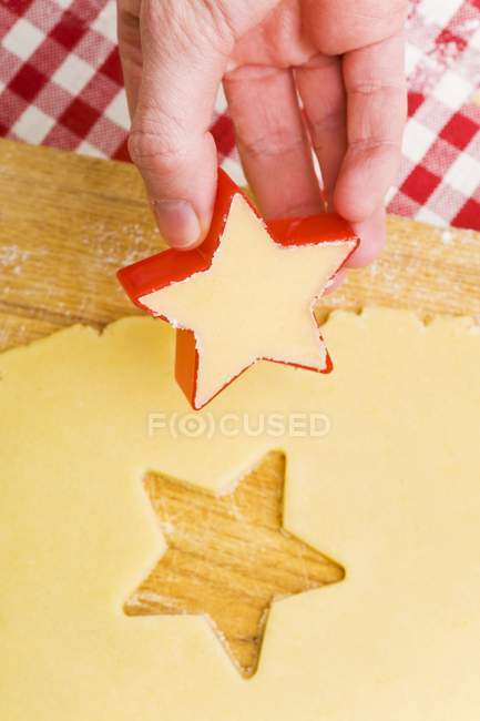 Vista close-up de mão segurando estrela em forma de cortador de biscoito sobre a massa de biscoito cortado — Fotografia de Stock