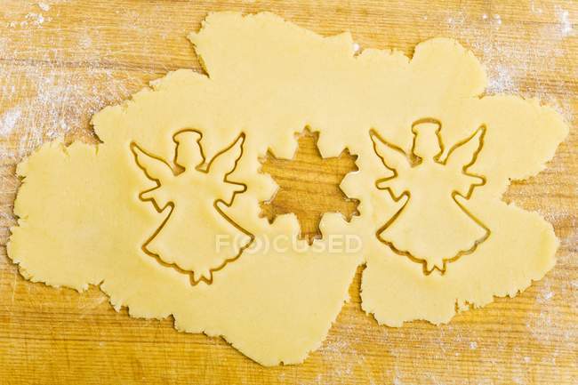 Closeup view of cut-out biscuits in dough on wooden surface — Stock Photo