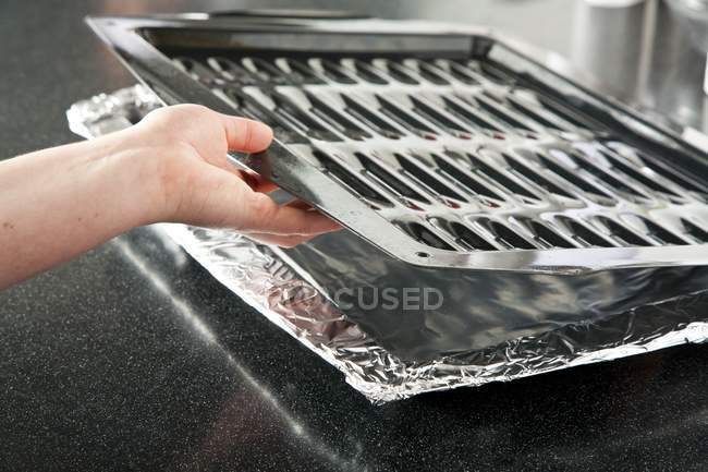 Closeup view of a hand placing a broiler pan on a foil lined pan — Stock Photo