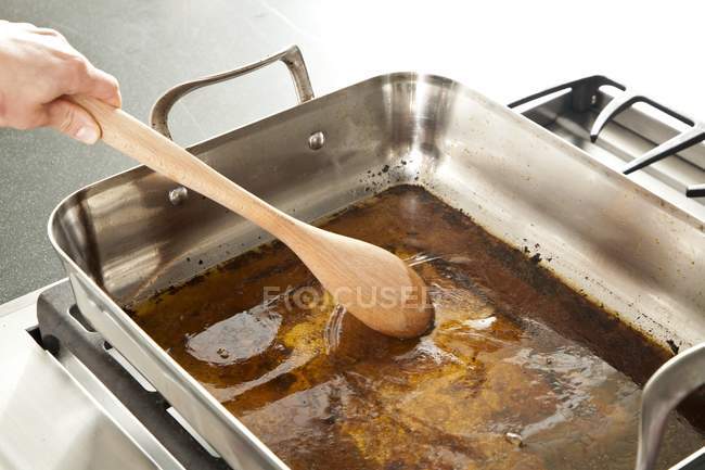 Elevated view of hand touching gravy with wooden spoon in metal dish — Stock Photo
