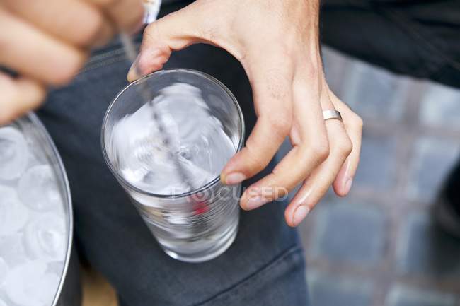 Vista de perto da pessoa mexendo cubos de gelo em vidro — Fotografia de Stock