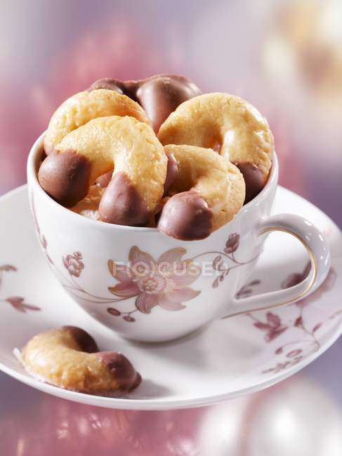 Closeup view of chocolate-dipped vanilla crescents in a cup and saucer — Stock Photo