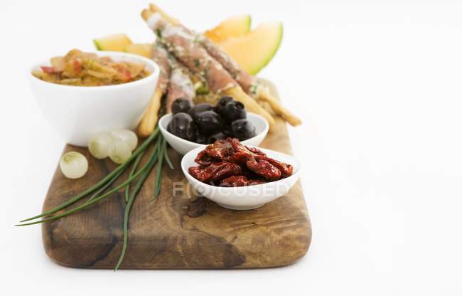 Antipasti dried tomatoes, olives, grissini, melon on wooden desk over wooden surface — Stock Photo