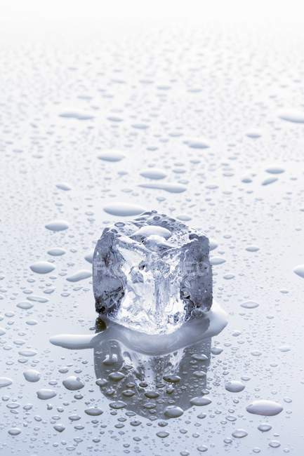 Vista de primer plano de un cubo de hielo sobre una superficie húmeda - foto de stock