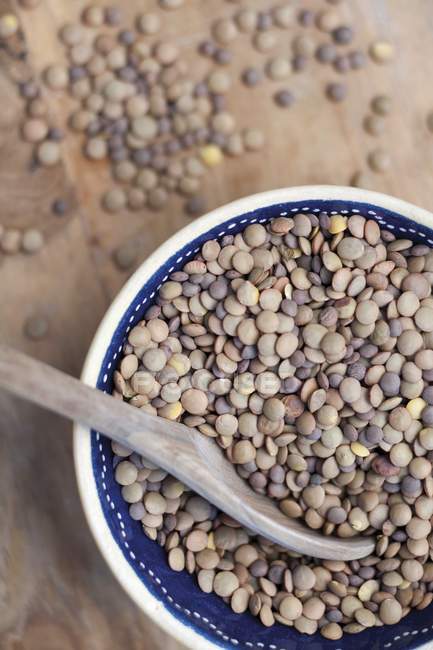 Closeup top view of brown lentils in a bowl with a wooden spoon — Stock Photo