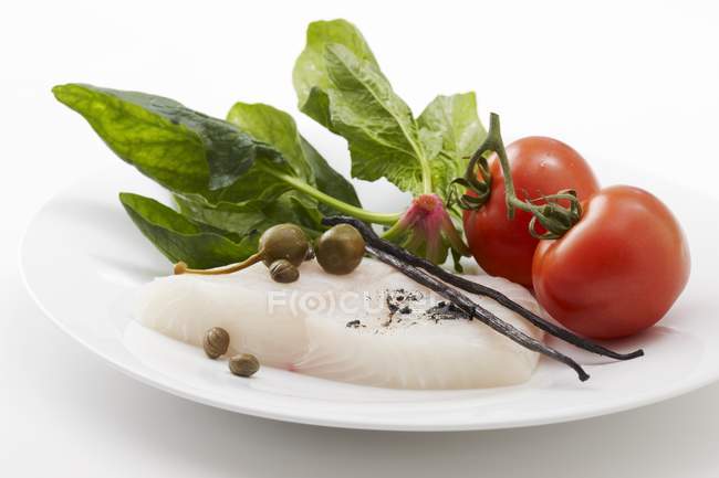 Палтус, шпинат, каперсы, ванильные стручки и помидоры на белой тарелке — стоковое фото