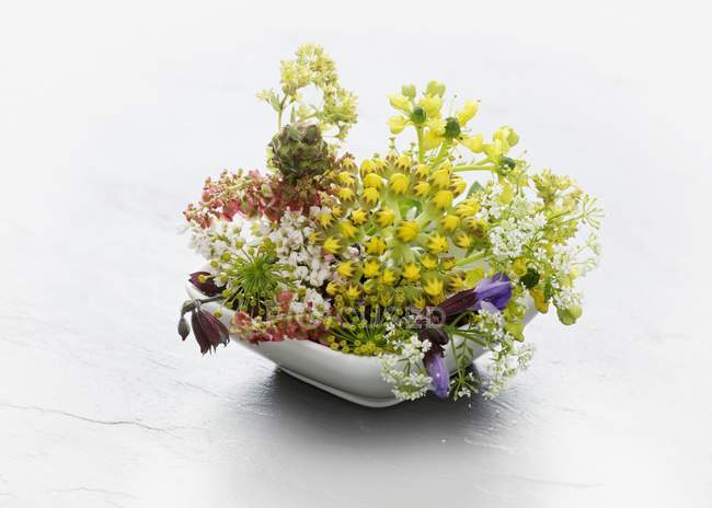 A bowl of wild herb flowers on white surface — Stock Photo