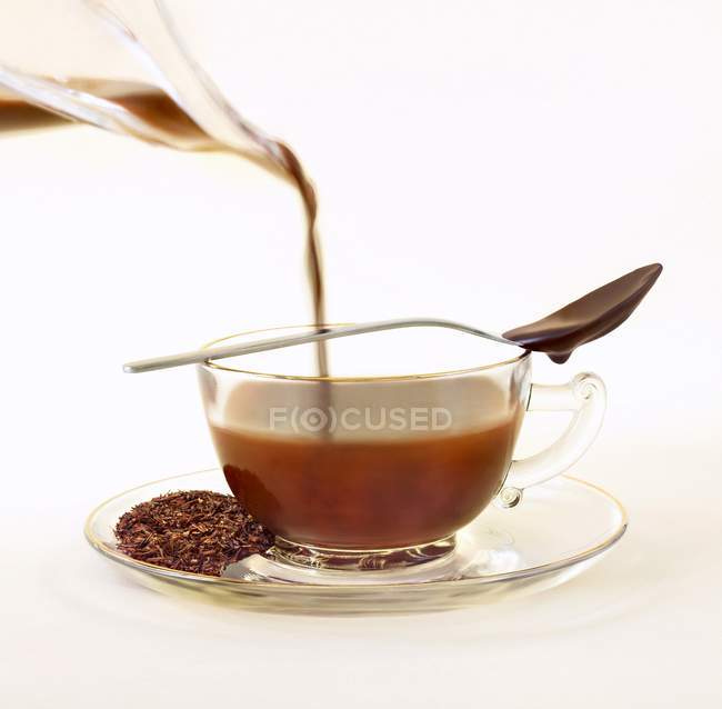 Vista ravvicinata di versare infuso di tè Rooibos a tazza con cucchiaio e cioccolato — Foto stock