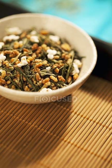 Вид крупным планом на зеленую чайную смесь Genmaicha в миске на бамбуковом подносе — стоковое фото