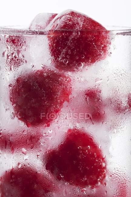 Glass of water with raspberry ice cubes — Stock Photo