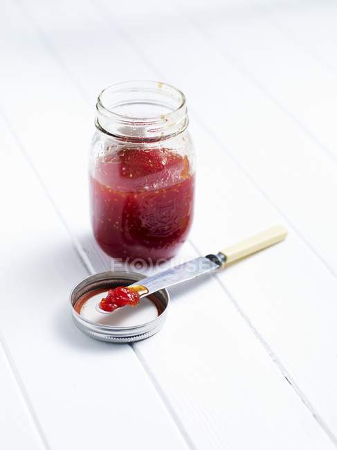 A jar of tomato chutney on white wooden surface — Stock Photo