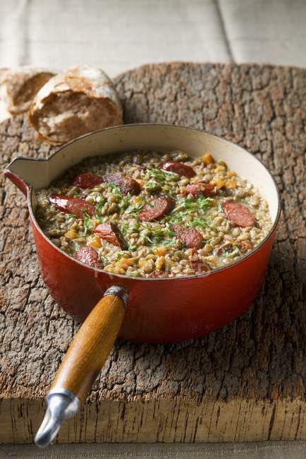 Lentil Stew with Sausages in red pot over wooden surface — Stock Photo