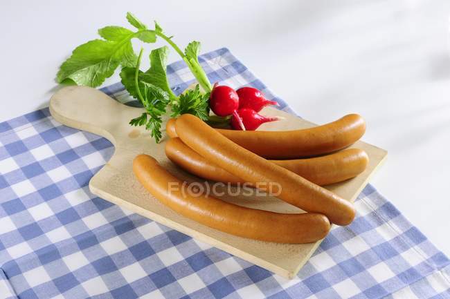 Hot dogs and radishes on a chopping board over towel — Stock Photo