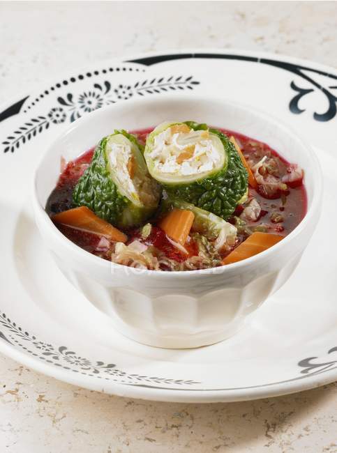 Borscht with savoy cabbage rolls in white bowl over plate — Stock Photo