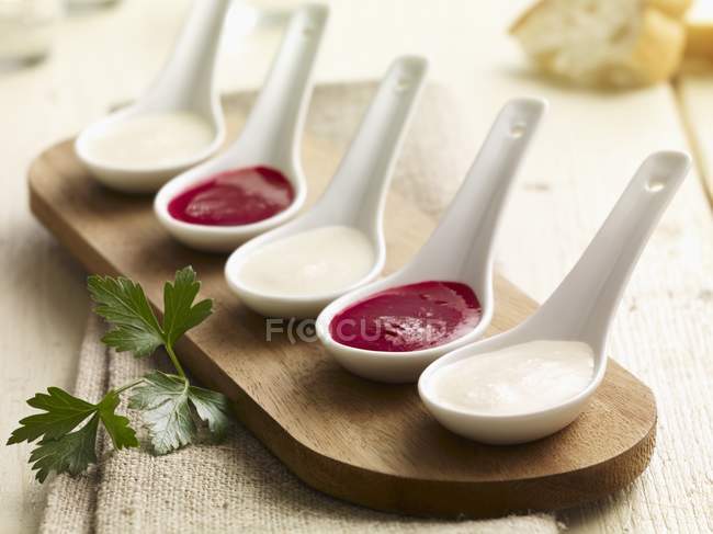 Kohlrabi y salsa de remolacha en cucharas de porcelana sobre la superficie de madera - foto de stock