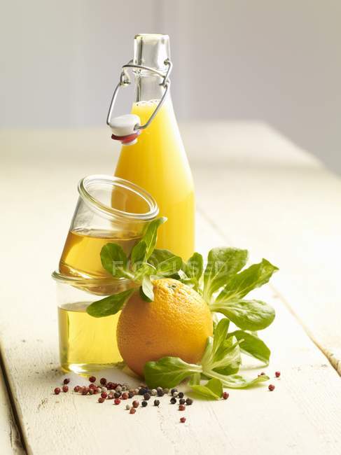 Vista de cerca de naranja con jugo, aceite, pimienta y hojas verdes - foto de stock