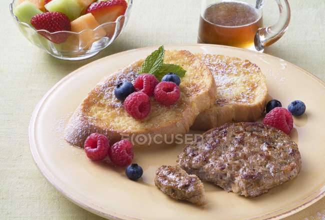 Closeup view of chicken sausage patty and French toasts with berries, syrup and fruit salad — Stock Photo