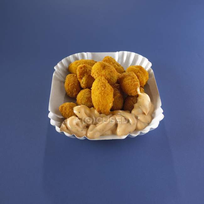 Vista de cerca de nuggets de pollo con inmersión en la placa de papel en la superficie azul - foto de stock