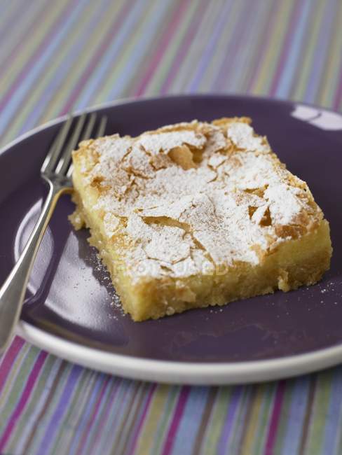 Primo piano vista di limone pezzo quadrato di torta su un piatto viola — Foto stock