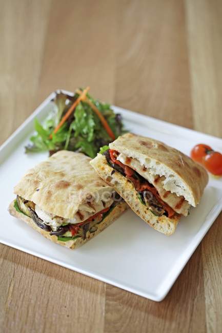A grilled vegetable panini  on white plate over wooden surface — Stock Photo