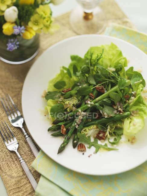 Insalata di foglie miste con asparagi verdi e noci su piatto bianco su asciugamano verde con forchetta — Foto stock