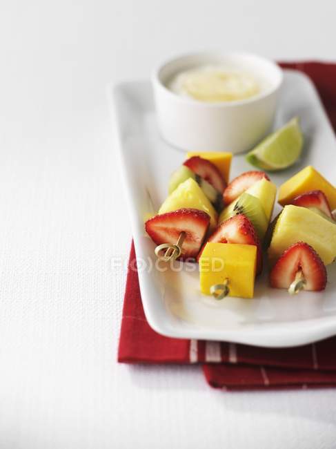 Vue rapprochée des brochettes de fruits avec bol sur assiette et serviette — Photo de stock