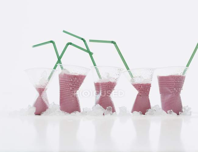 Vista de cerca de daiquiris de fresa congelados en tapas de plástico con pajitas - foto de stock