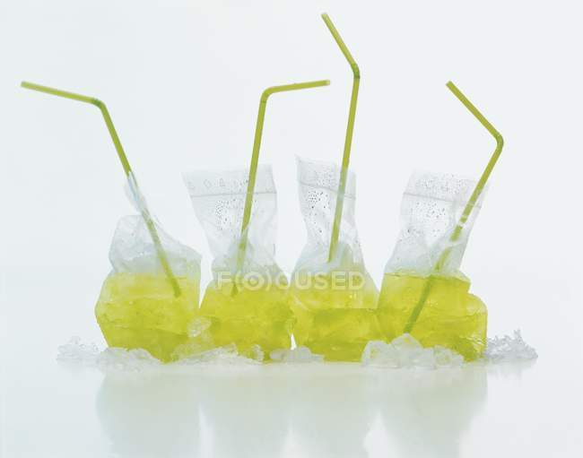 Вид крупным планом кислых яблочных напитков в пластиковых пакетах с соломинками и льдом — стоковое фото