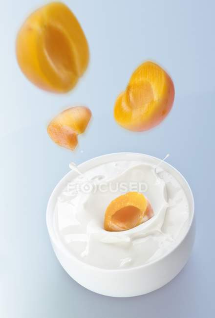 Peaches falling into yogurt — Stock Photo