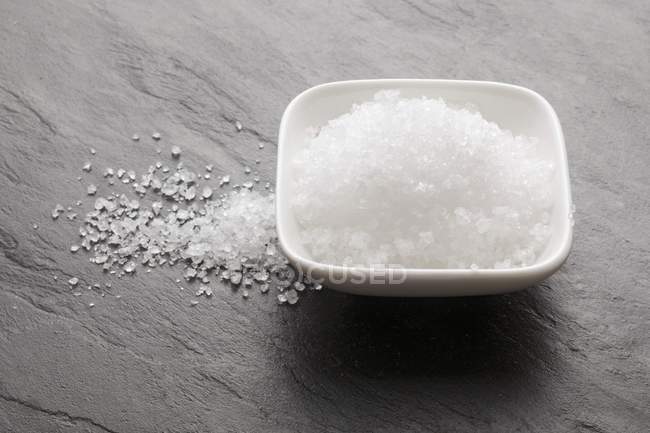 Closeup view of Fleur de sel in a bowl and on a slate surface — Stock Photo