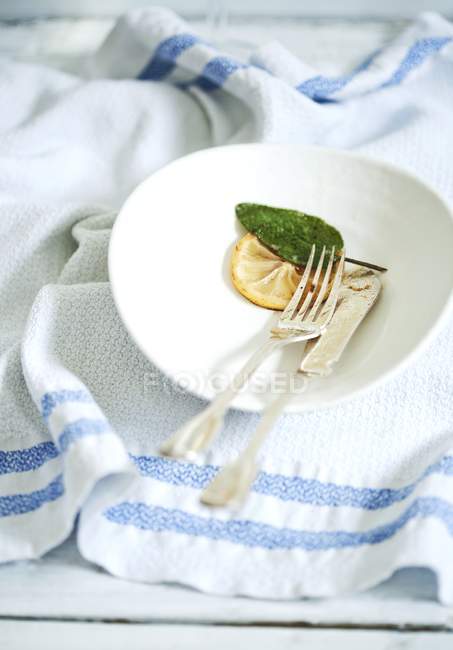 Vista close-up de faca com garfo, limão e folha de sálvia na placa branca — Fotografia de Stock