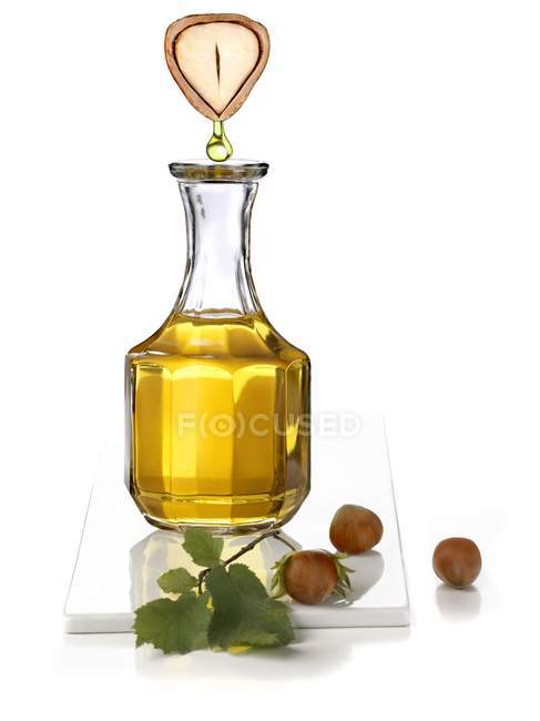 Closeup view of hazelnut oil dropping from big halved hazelnut to carafe — Stock Photo