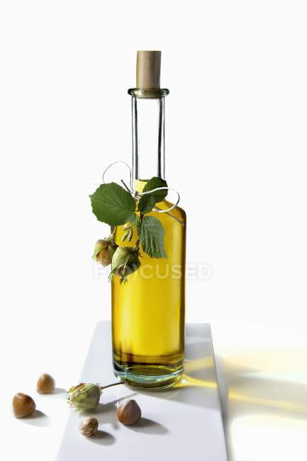 Une huile de noisette dans une bouteille et noisettes sur fond blanc — Photo de stock