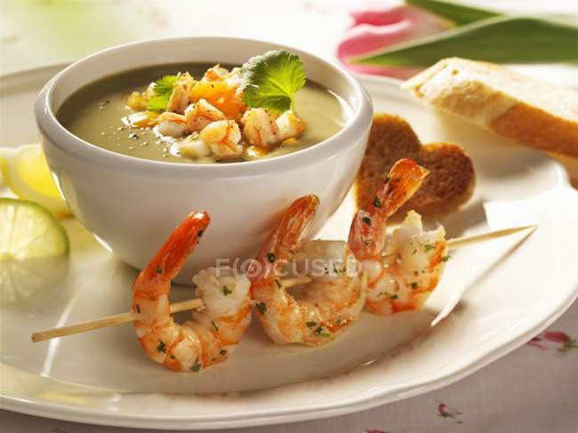 Sopa de aguacate con brochetas de camarón en un tazón sobre el plato - foto de stock